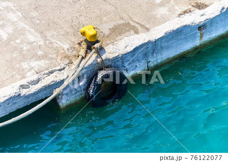 Yellow mooring bollard with rope on grey concrete pier Yellow mooring bollard with rope on grey concrete pier 76122077