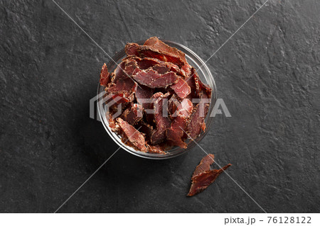 Bowl with jerky meat on a dark background, top view 76128122