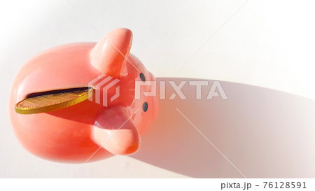 Top view over pink piggy bank with slot and inserted coin, on white background, savings and investment concept, copy space, space for text Top view over pink piggy bank with slot and inserted coin, on white background, savings and investment concept, copy space, space for text 76128591