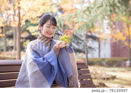 秋の公園でブドウを持つ女性（笑顔） 76130997