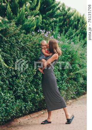 a small child sits on the mother's hands. momy's daughter is on vacation. tropical leaves. Travel to hot countries a small child sits on the mother's hands. momy's daughter is on vacation. tropical leaves. Travel to hot countries 76135706