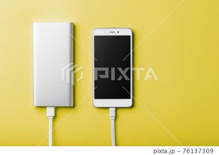 Smartphone charging with power bank by wire on yellow background. Smartphone charging with power bank by wire on yellow background. 76137309