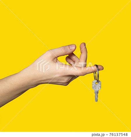On finger of woman hand hangs key on bright yellow background. 76137548