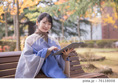 秋の公園でタブレットPCを使う女性（笑顔） 76138008