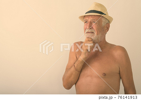 Studio shot of handsome senior bearded man thinking while looking up and wearing hat shirtless 76141913