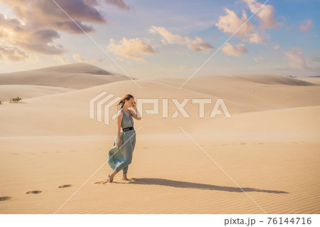 Young beautiful woman traveling in the desert. Sandy dunes and blue sky on sunny summer day. Travel, adventure, freedom concept. Tourism reopens after quarantine COVID 19 Young beautiful woman traveling in the desert. Sandy dunes and blue sky on sunny summer day. Travel, adventure, freedom concept. Tourism reopens after quarantine COVID 19 76144716