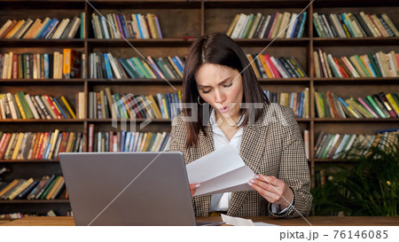 Dark haired woman opens letter and touches cheek with shock Dark haired woman opens letter and touches cheek with shock 76146085