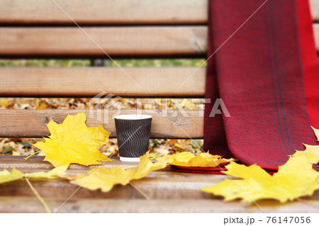 Bench with cup of coffee, scarf and dry leaves in the city park in autumn. Bench with cup of coffee, scarf and dry leaves in the city park in autumn. 76147056