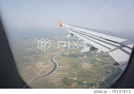 Wing of airplane over the clouds. View from the window of an airplane flying. Flying in the sky above the landscape Wing of airplane over the clouds. View from the window of an airplane flying. Flying in the sky above the landscape 76147673