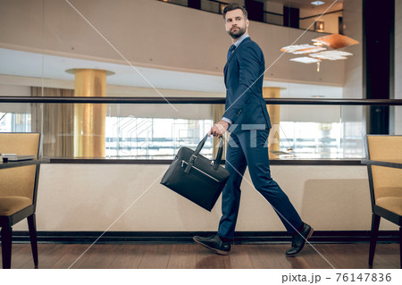 Buisnessman in a blue suit holding a suitcase walking fast Buisnessman in a blue suit holding a suitcase walking fast 76147836