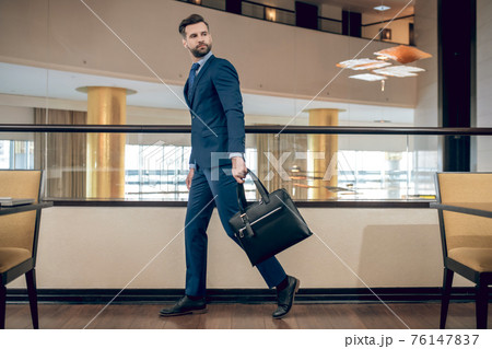 Buisnessman in a blue suit holding a suitcase walking fast 76147837