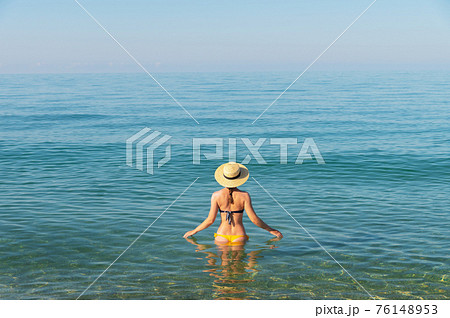 a slender young woman in a swimsuit and a hat stands waist-deep in the sea water on a sunny day a slender young woman in a swimsuit and a hat stands waist-deep in the sea water on a sunny day 76148953