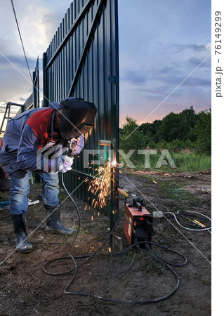 welding of a metal profile to a fence, process of welding close-up, the worker in a protective helmet against sparks. 76149299