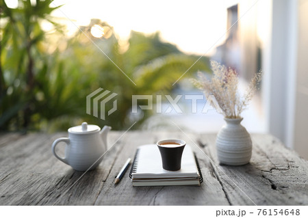 Small black tea cup and white kettle and dry flower vase and notebook on wooden table 76154648