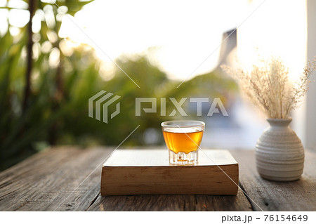 Tea in transparent cup on thick brown book on wooden table 76154649