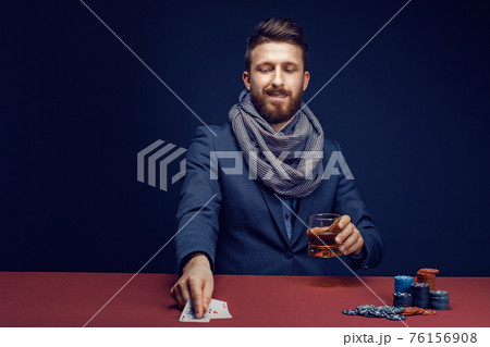 Stylish bearded Man in suit and scarf playing in dark casino, smoking cigar, drink whiskey Stylish bearded Man in suit and scarf playing in dark casino, smoking cigar, drink whiskey 76156908