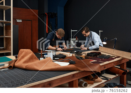 leather craftsmen working making measupenets in patterns at table in workshop studio 76158262