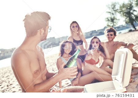 Enjoying carefree time with friends. Cheerful young people spending nice time together while sitting on the beach and drinking beer 76159431