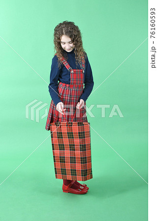 Child with a red packet isolated on green background. Little beauty shopaholic. Holiday present, shopping. Child with a red packet isolated on green background. Little beauty shopaholic. Holiday present, shopping. 76160593