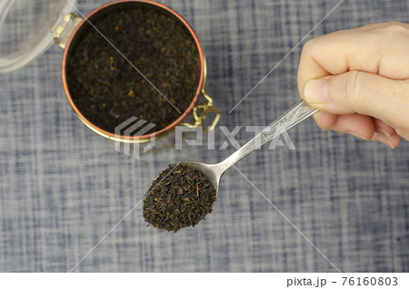 A woman's hand holds a metal spoon with dried tea leaves. A woman's hand holds a metal spoon with dried tea leaves. 76160803