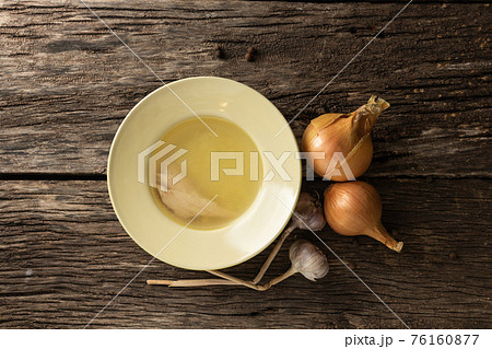 Bowl with clear rich broth. White crockery on an aged wooden table. Vegetables - onions, garlic, spices Bowl with clear rich broth. White crockery on an aged wooden table. Vegetables - onions, garlic, spices 76160877