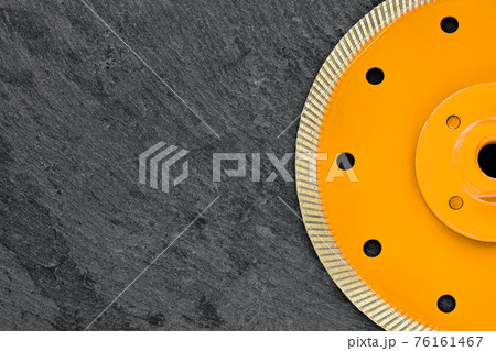 Half of a yellow diamond cutting wheel with a threaded nut on a dark gray granite background, the concept of stone processing in the interior and construction. 76161467