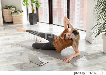 Adult caucasian woman lies on the floor and practice workout at home in front of the laptop, online fitness class, selective focus. 76161565
