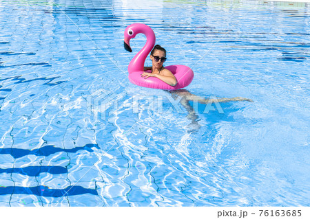 Summer sale. Young sexy woman in bikini swimsuit, sunglasses with pink flamingo relaxing in blue pool water. Summer luxury vacation in spa resort pool. Summer sale. Young sexy woman in bikini swimsuit, sunglasses with pink flamingo relaxing in blue pool water. Summer luxury vacation in spa resort pool. 76163685