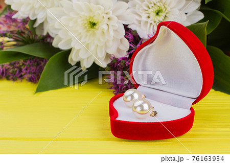 Heart-shaped box with earring and flowers. Heart-shaped box with earring and flowers. 76163934