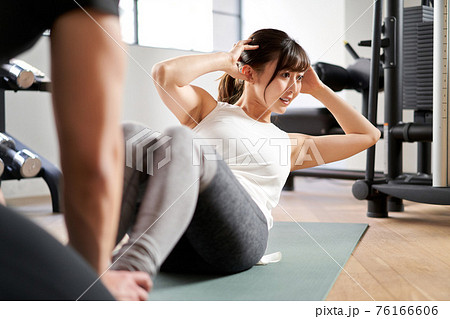 パーソナルトレーナーの指導で腹筋運動をするアジア人女性 76166606