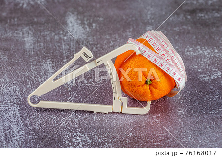 Orange wrapped with measuring tape and caliper on a gray concrete background. 76168017