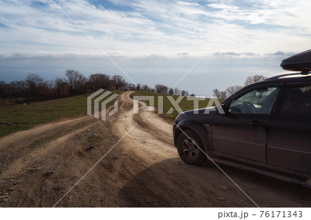 A gravel road leading toward horizon. Spectacular view on the sea and blue sky in the evening. Offroad 4x4 car 76171343