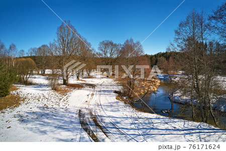 Early spring landscape with melting snow. Dirt rural road, wood, ice and snow panorama. Early spring landscape with melting snow. Dirt rural road, wood, ice and snow panorama. 76171624