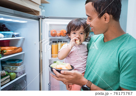 father and daughter open refrigerator at home having some fresh fruit together father and daughter open refrigerator at home having some fresh fruit together 76175767