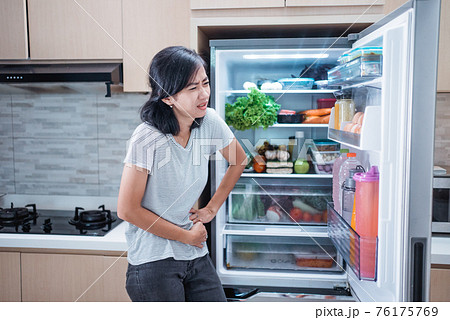 starving young asian woman hold her belly while open the fridge door looking for food starving young asian woman hold her belly while open the fridge door looking for food 76175769