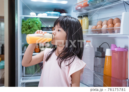 asian girl open fridge door drinking a bottle of juice 76175781