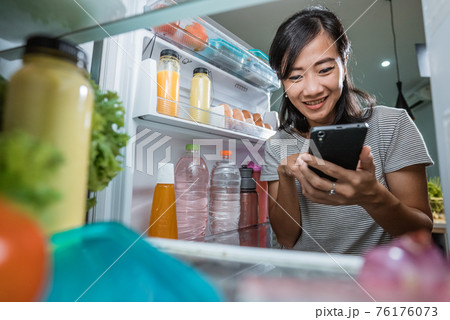 woman using her smartphone to buy groceries while open her fridge 76176073