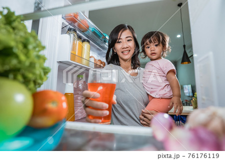 mother carrying her daughter while taking a glass of juice inside the fridge mother carrying her daughter while taking a glass of juice inside the fridge 76176119