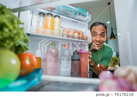 excited young asian man opening the fridge door 76176216