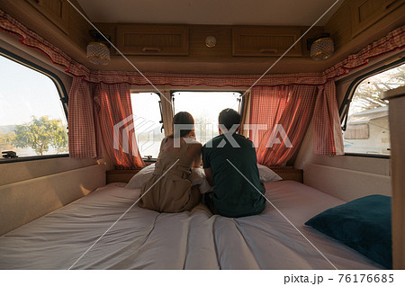 Young couple sitting and taking a view on mattress inside of camper van Young couple sitting and taking a view on mattress inside of camper van 76176685