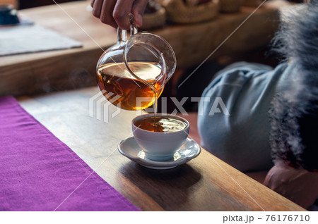 Hand pouring hot tea from jug into white teacup on the table 76176710