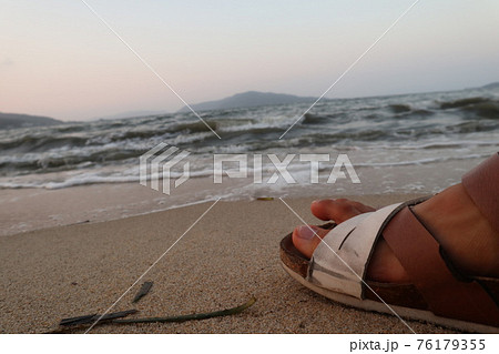 夕暮れ時の砂浜でビーチサンダルを履き休憩の写真素材