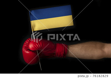 Boxer hand holds flag of Ukraine. Boxing glove with the Ukraine flag. Black background. Boxer hand holds flag of Ukraine. Boxing glove with the Ukraine flag. Black background. 76182829