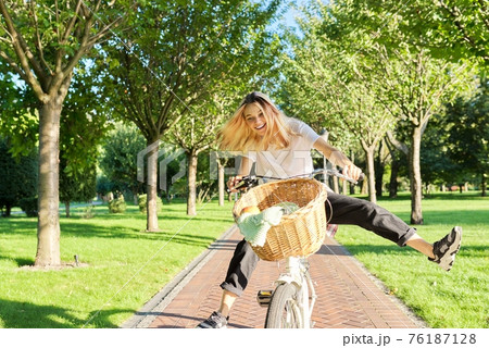 Happy young woman riding bike on road in park, beautiful hipter teenager having fun and laughing 76187128