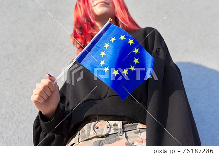 Female student teenager with EU flag in hand, gray outdoor wall background Female student teenager with EU flag in hand, gray outdoor wall background 76187286