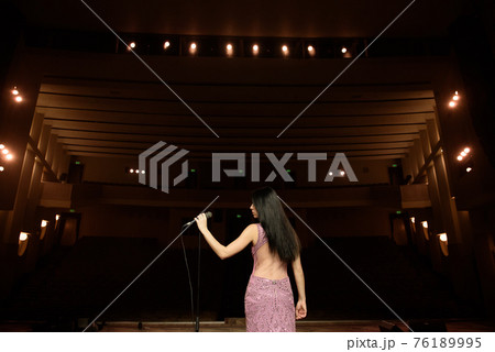 Beautiful singer against the auditorium. Back view girl in long gown performing on stage. Beautiful singer against the auditorium. Back view girl in long gown performing on stage. 76189995