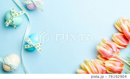 Easter eggs background. Colorful egg with tape ribbon, spring tulips, feathers on pastel blue background in Happy Easter decoration. Foil minimalist egg design, modern top view template. Easter eggs background. Colorful egg with tape ribbon, spring tulips, feathers on pastel blue background in Happy Easter decoration. Foil minimalist egg design, modern top view template. 76192904