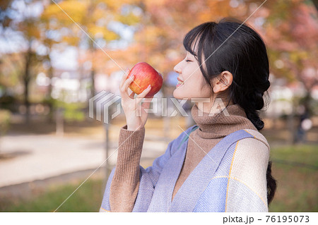 秋の公園でりんごを食べる女性（横顔） 76195073