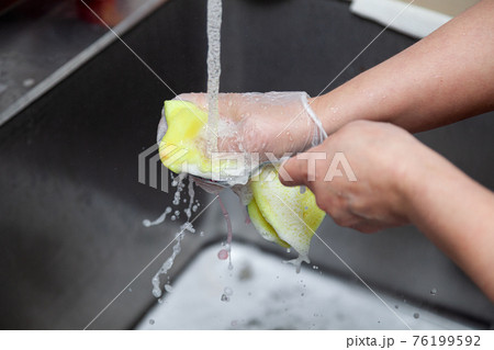 Dishwasher in uniform washes griddle with foam and sponge under the tap water Dishwasher in uniform washes griddle with foam and sponge under the tap water 76199592