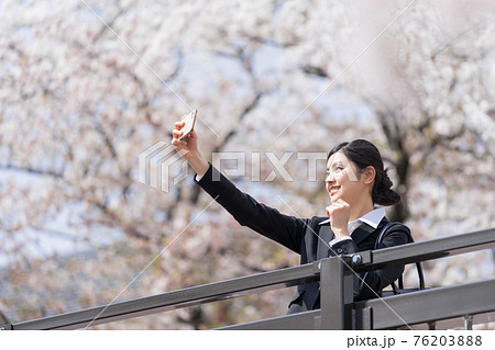 橋の上から桜並木を背景に自撮りするスーツの女性 ビジネスウーマン 橋の上から桜並木を背景に自撮りするスーツの女性 ビジネスウーマン 76203888